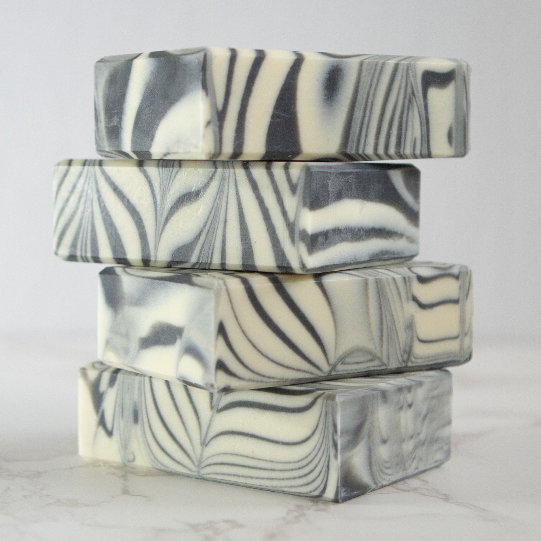 4 bars of Peppermint and Tea Tree soap with a black and white swirled design stacked on top of one another.