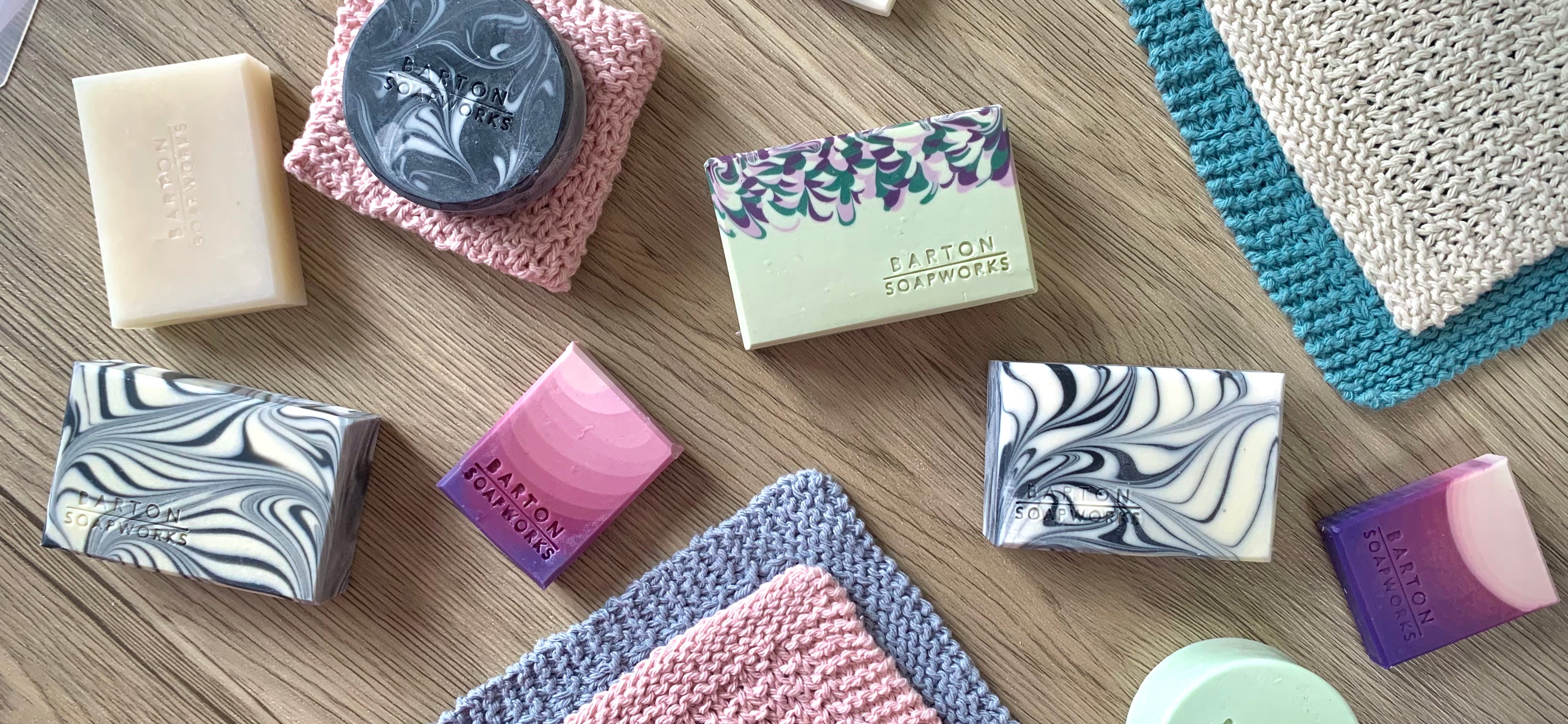 Selection of beautiful artisan soap in various designs and colours with hand knitted face cloths laid out on a wooden surface 