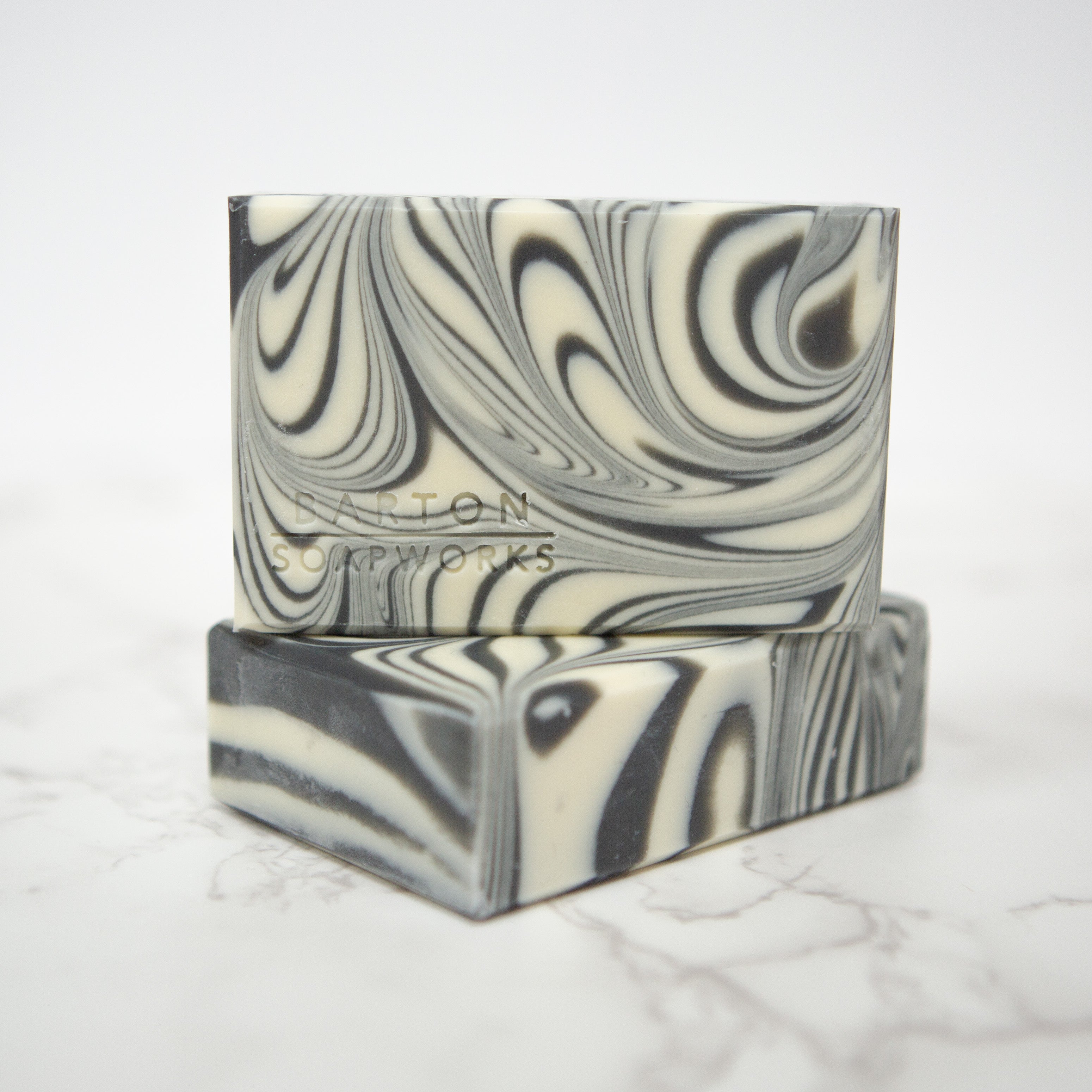 a bar of Barton Soapworks soap with a black and white swirl design placed on top of another. 